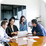 Four professionals discuss Corporate Governance strategy around a laptop and documents in an office meeting.