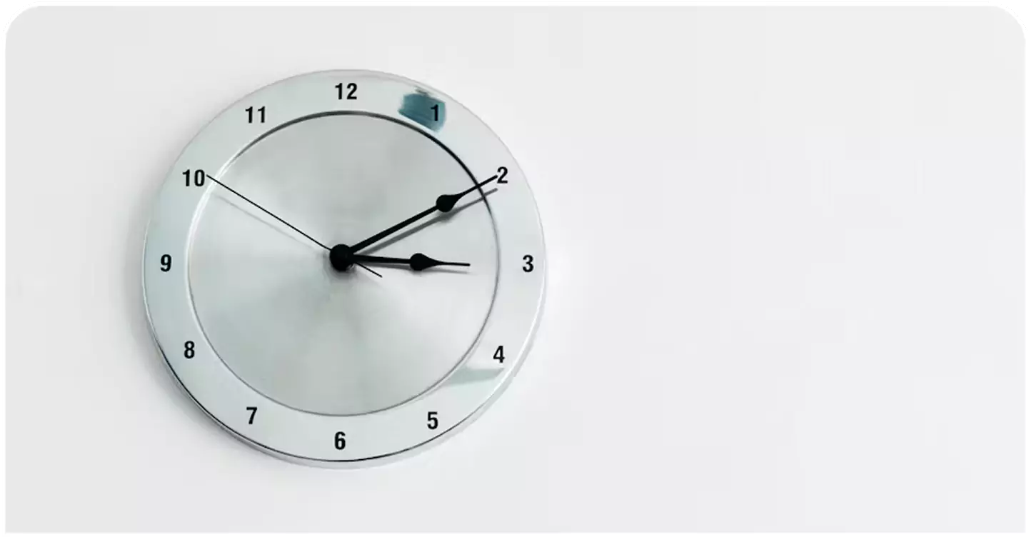 Round silver wall clock with black hands on a minimalist white wall, symbolizing efficient deadline tracking.