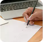 A hand writing documents on a paper with a pen, laptop in the background. Symbolizing a Foundation for Future Filings.