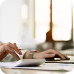 Hands using a calculator and a laptop for financial management and ensuring Ongoing Compliance.