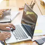Hands typing on a silver laptop, with another person using a tablet, reflecting collaborative work and Regulatory Compliance efforts.