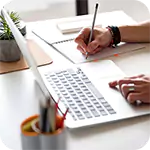 Person working at a desk, writing in a notebook with a laptop open. Meeting strict requirements for productivity.